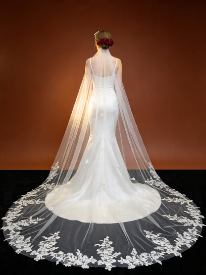 Studio shot of bride wearing airy floral lace trimmed cathedral veil, backlit to show sheer tulle and glowing floral lace hem