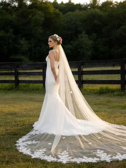 Bride wearing airy floral lace trimmed cathedral wedding veil in a forest setting, showing the full lace hem and sheer tulle